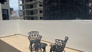 A rooftop terrace with two ornate metal chairs and a small table, surrounded by a white wall and a view of a building under construction. - Apartahotel Alvear (Santo Domingo)