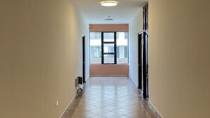 A narrow hallway with a tiled floor, a ceiling light, and a window at the end. - Apartahotel Alvear (Santo Domingo)