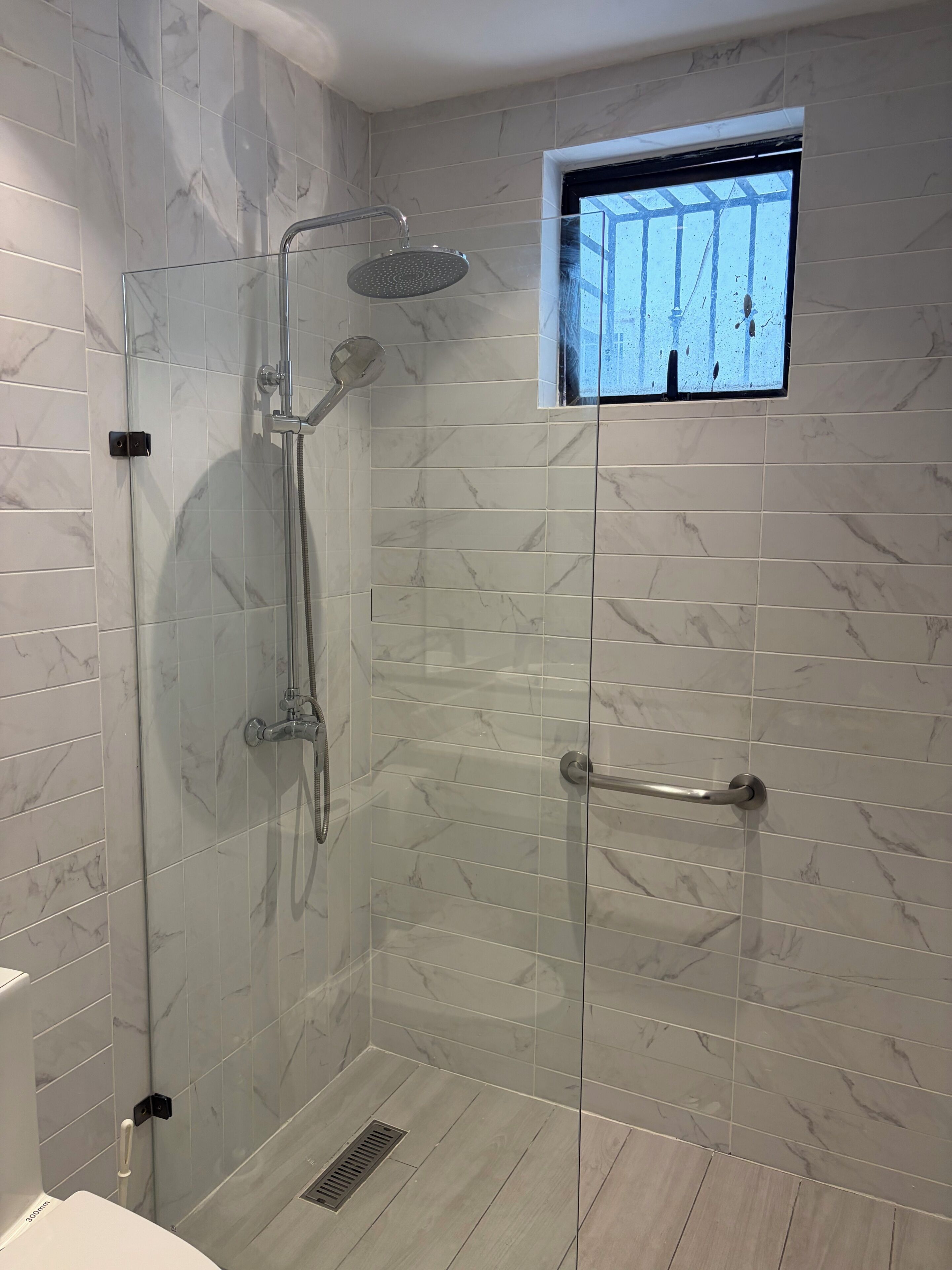 A glass-enclosed shower with a handheld showerhead and a handheld showerhead with a rain shower attachment.