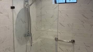 A glass-enclosed shower with a handheld showerhead and a handheld showerhead with a rain shower attachment.