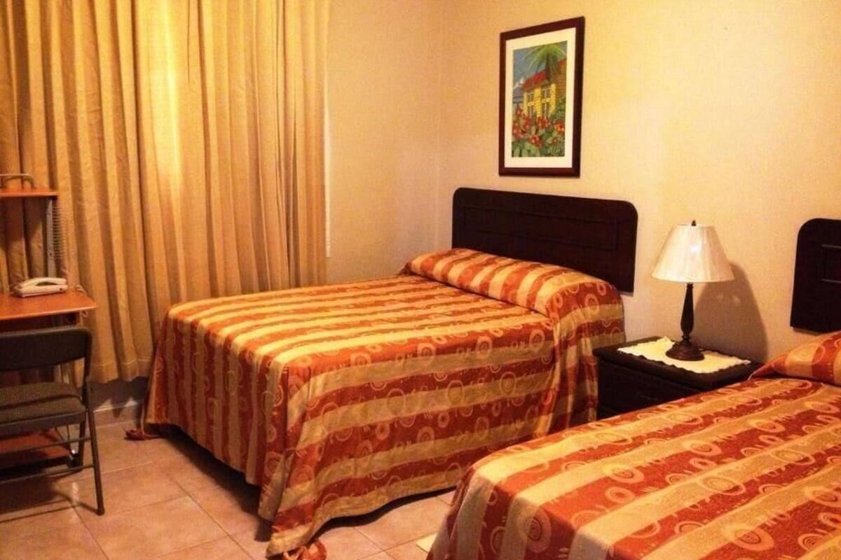 A hotel room with two beds, a desk, a chair, a lamp, and a painting on the wall.