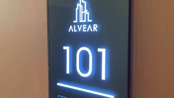 Un panneau numérique affichant le chiffre 101 et le mot « ALVEAR » est fixé à un mur.