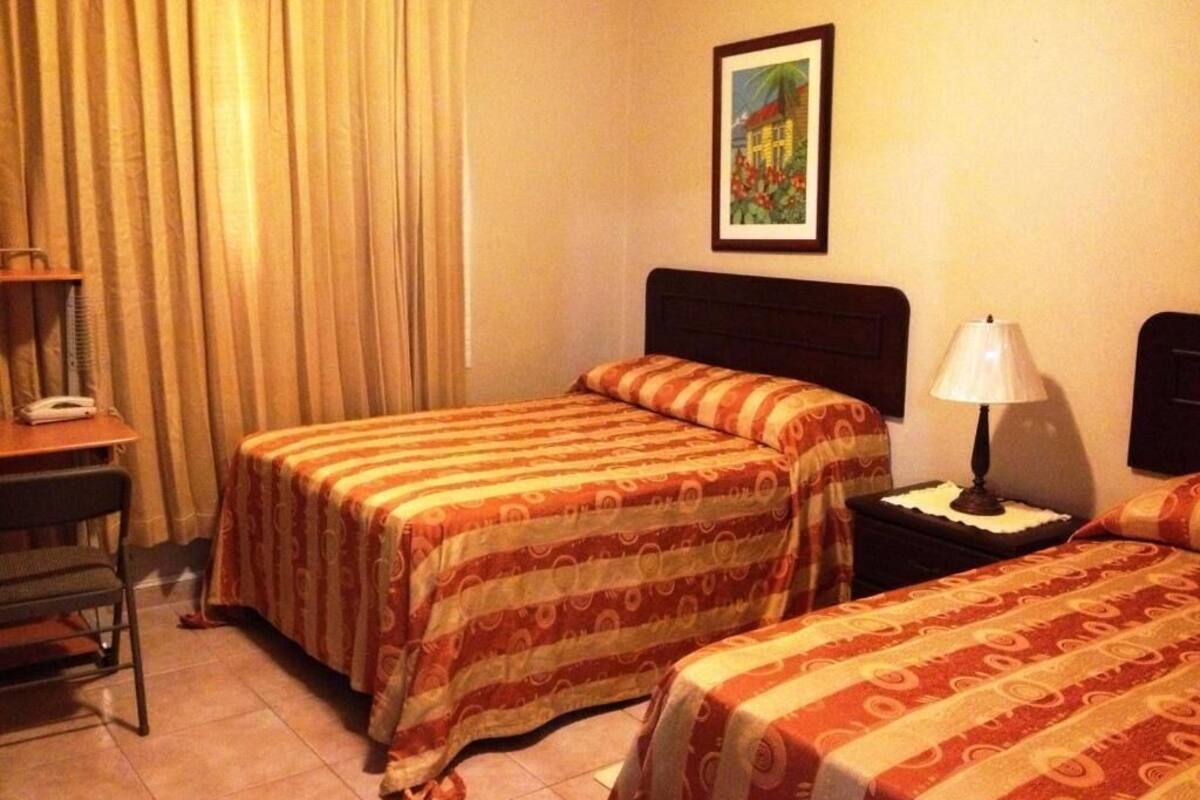 A hotel room with two beds, a desk with a telephone, a lamp, and a painting on the wall.