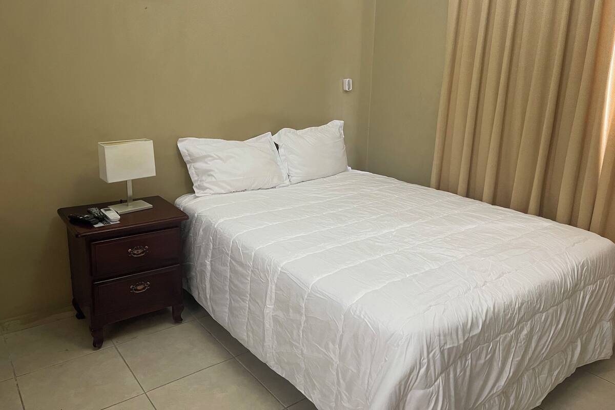 A hotel room with a bed, a nightstand, a lamp, and a curtain.