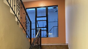 A staircase with a black metal railing and brown tiled steps leading to a landing with a large window. - Apartahotel Alvear (Santo Domingo)