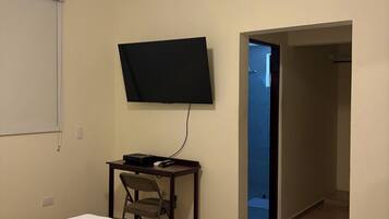 Quarto de hotel com cama, escrivaninha, cadeira, televisão de tela plana e ventilador de teto.
