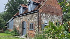 Een stenen huis met schuin dak, een grijze deur en een klein raam.