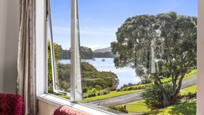 A room with a large window overlooking a lake, a tree, and a road.