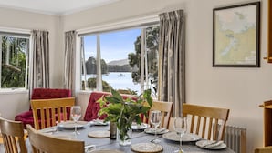 A dining area with a table set for four, large windows with curtains, a map on the wall, and a view of a body of water.