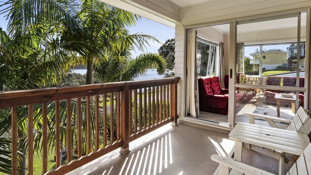A balcony with a wooden railing, a red chair, and a white table.