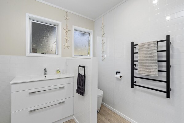 A modern bathroom with white tiles, a sink, a toilet, and a towel rack.