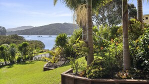 A coastal garden with palm trees, a grassy lawn, and a view of boats on the water.