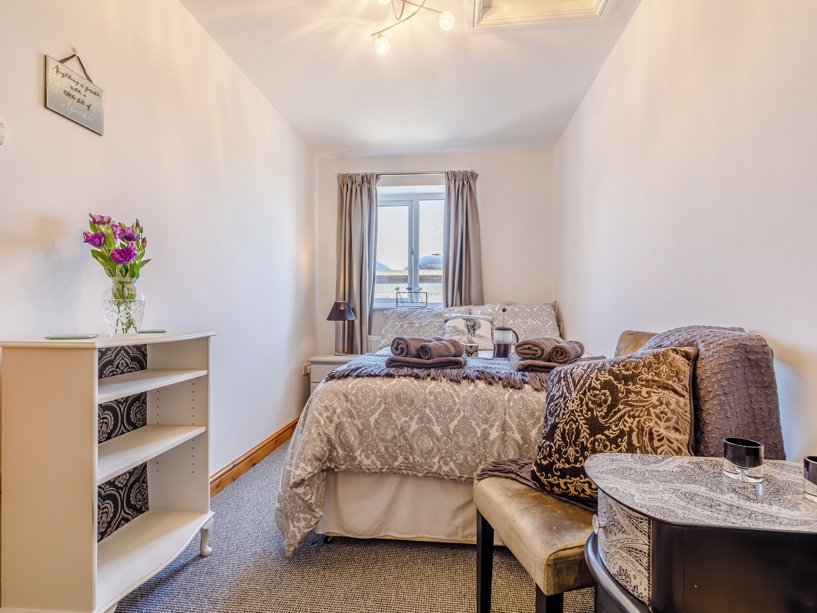 A neatly arranged bedroom with a bed, bedside table, and a small round table with a lamp.