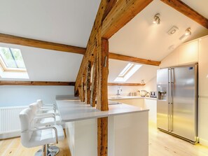 A modern kitchen with a central island, wooden beams, skylights, and a stainless steel refrigerator.