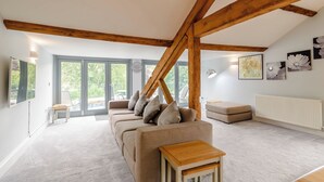 En rummelig stue med højt til loftet, træbjælker, en sofasæt, et lille træbord og en radiator.