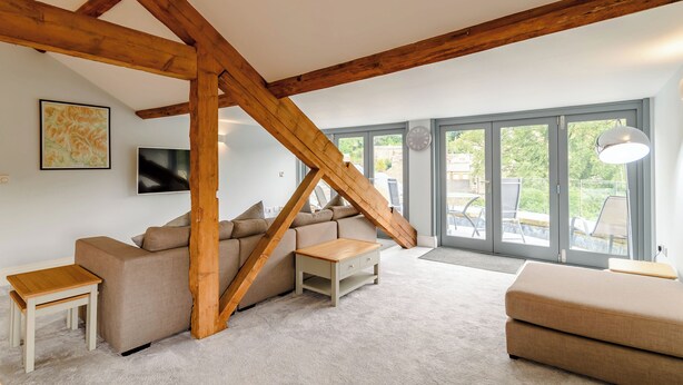 En stue i loftstil med synlige træbjælker, en sofa, et sofabord og udsigt gennem store skydedøre.