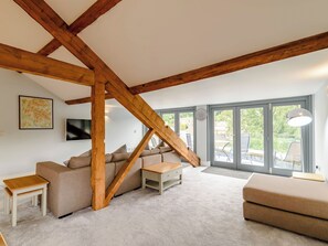 En stue i loftstil med synlige træbjælker, en sofa, et sofabord og udsigt gennem store skydedøre.