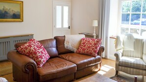 A living room with a brown leather sofa, a white armchair, and a painting on the wall. - 3 bedroom accommodation in Shilbottle (Shilbottle)