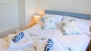 A neatly made bed with floral pillows and towels, a bedside lamp, and a shelf with decorative items. - 3 bedroom accommodation in Shilbottle (Shilbottle)