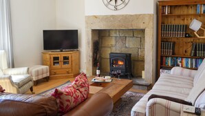 A cozy living room with a stone fireplace, a flat-screen TV, leather sofas, and a bookshelf filled with books. - 3 bedroom accommodation in Shilbottle (Shilbottle)