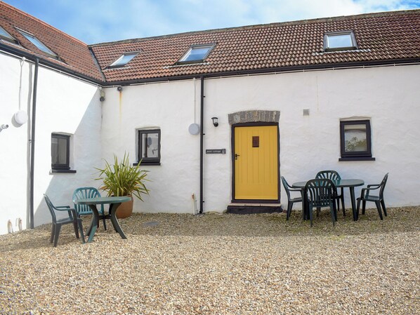 A building with a yellow door, a small window, and a table with chairs in front.