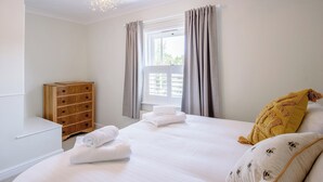 Un dormitorio con cama, cómoda de madera, ventana con cortinas y candelabro.