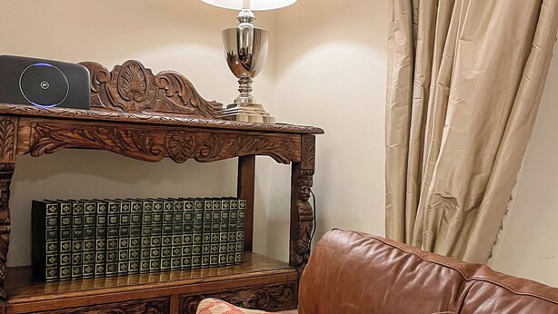 Een houten bijzettafeltje met een lamp, een stapel boeken en een lijst met foto aan een muur.