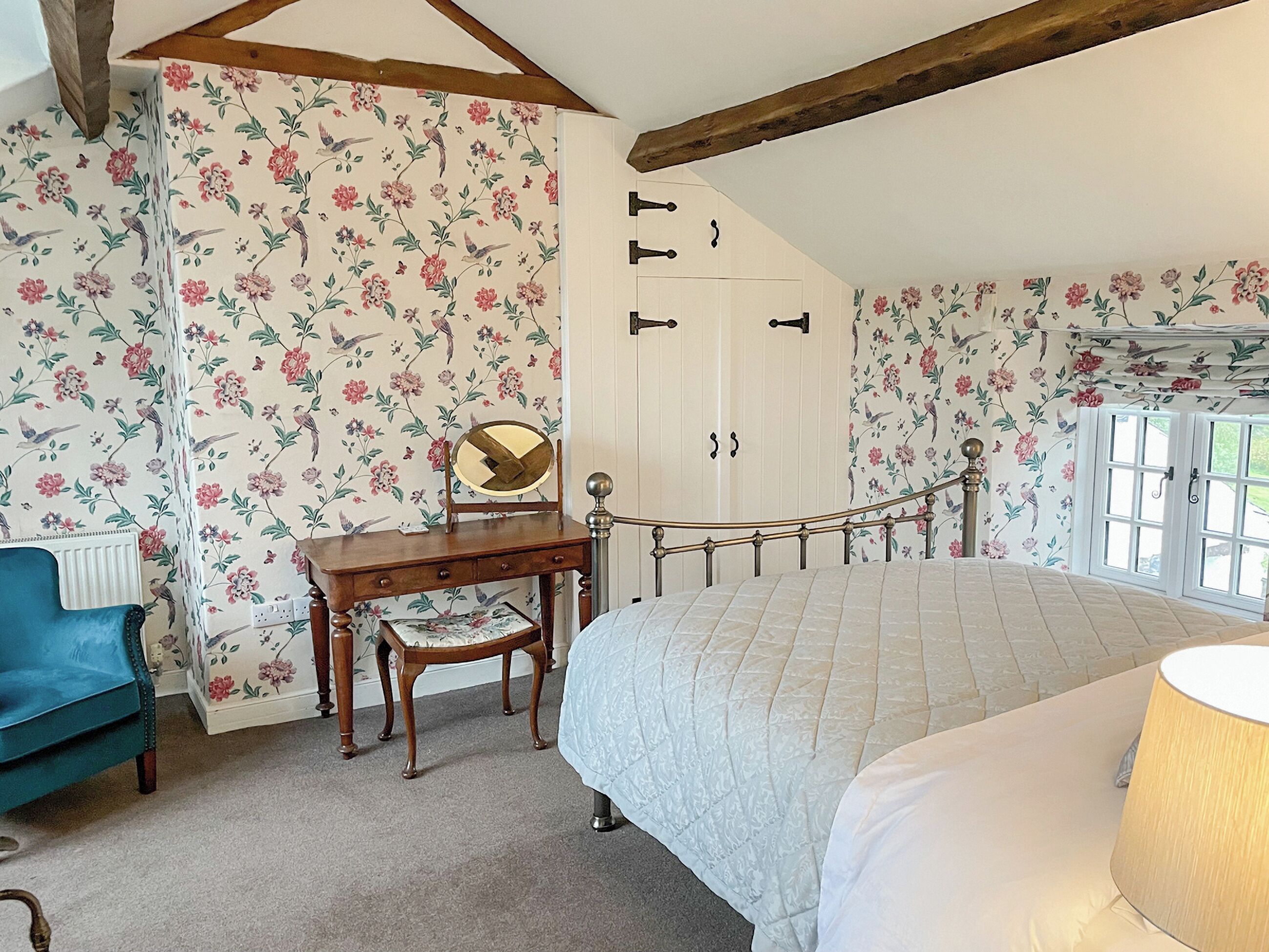 A bedroom with a bed, a desk with a mirror, a blue chair, and a wardrobe.