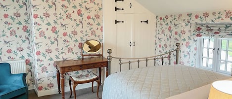 A bedroom with a bed, a desk with a mirror, a blue chair, and a wardrobe.