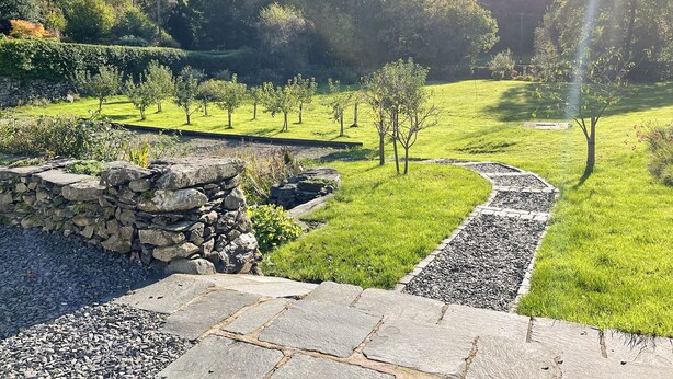 A landscaped garden with a stone wall, a gravel path, and a grassy area with trees. - 3 bedroom accommodation in Bowness on Windermere (Bowness on Windermere)