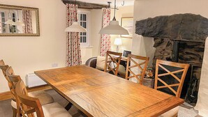 Een eetkamer met een houten tafel, stoelen, een open haard en een spiegel.