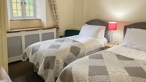 Een kamer met twee bedden, een raam met gordijnen, een bedlampje en een radiator.