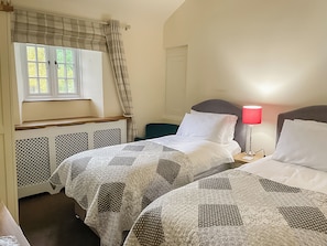 Une chambre avec deux lits, une fenêtre avec des rideaux, une lampe de chevet et un radiateur.