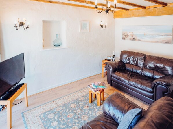 A living room with a leather sofa, a TV on a wooden stand, a small table with books, a blue vase, and a painting on the wall.