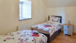 A bedroom with two beds, a window, a bedside table, and a radiator.