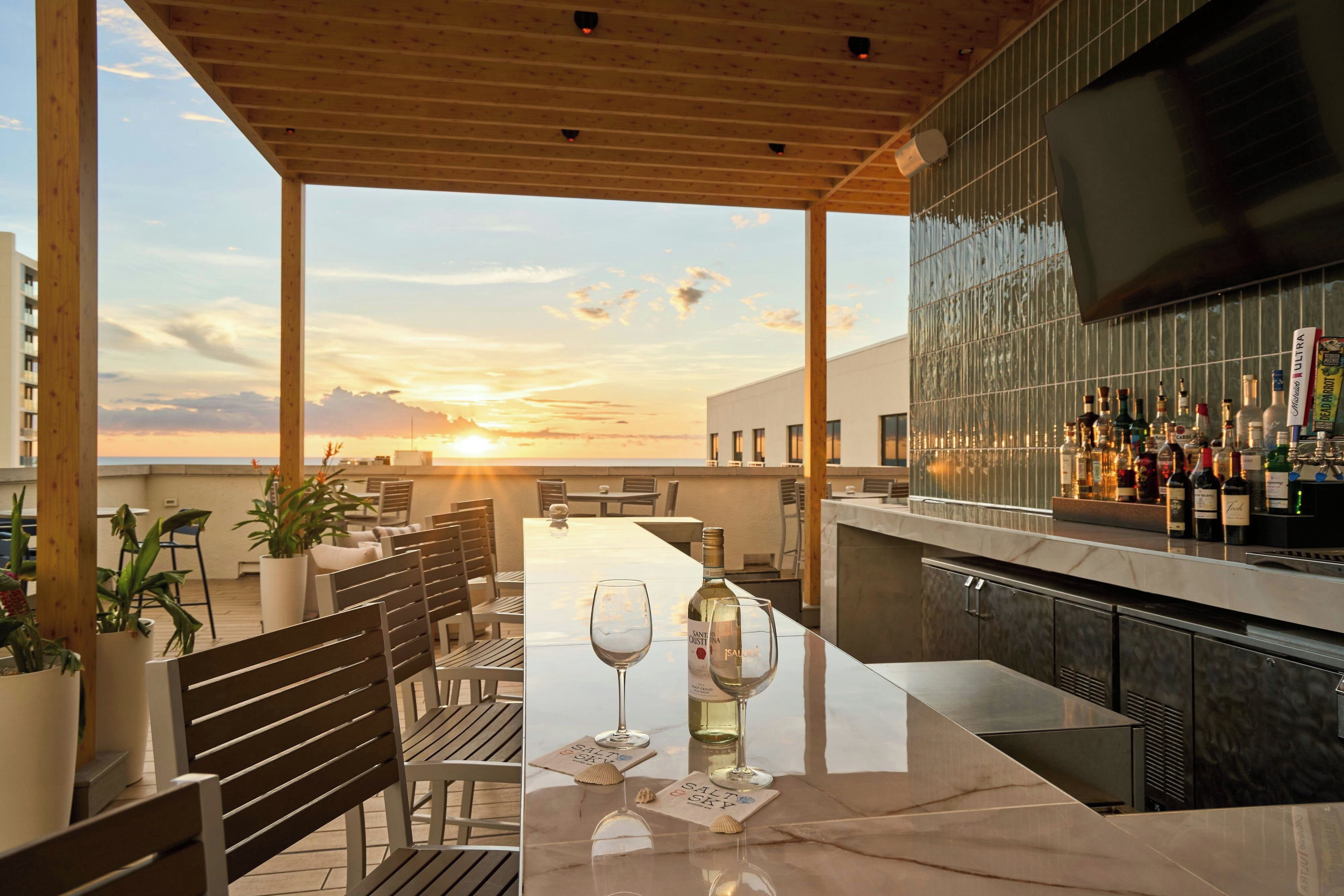Een terras met bar, uitzicht op de zonsondergang, zitgedeeltes en verschillende flessen.