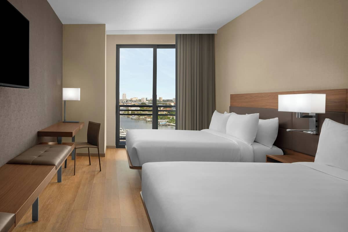 Habitación de hotel con dos camas, un escritorio, una silla, un televisor y vistas a la ciudad.