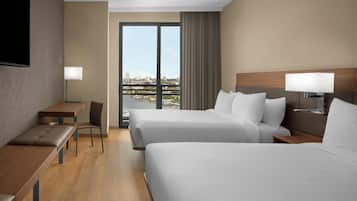 Habitación de hotel con dos camas, un escritorio, una silla, un televisor y vistas a la ciudad.