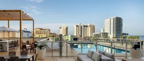 A rooftop pool area with outdoor seating, a pool, and city views.