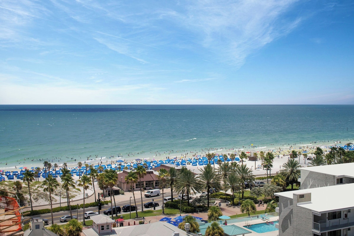 Vista de una playa con piscina y un edificio con balcones.