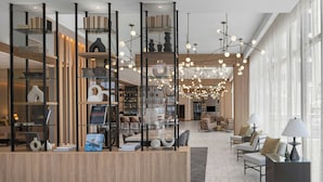 Un moderno vestíbulo de hotel con mostrador de recepción, zona de estar y un amplio ventanal que proporciona luz natural.