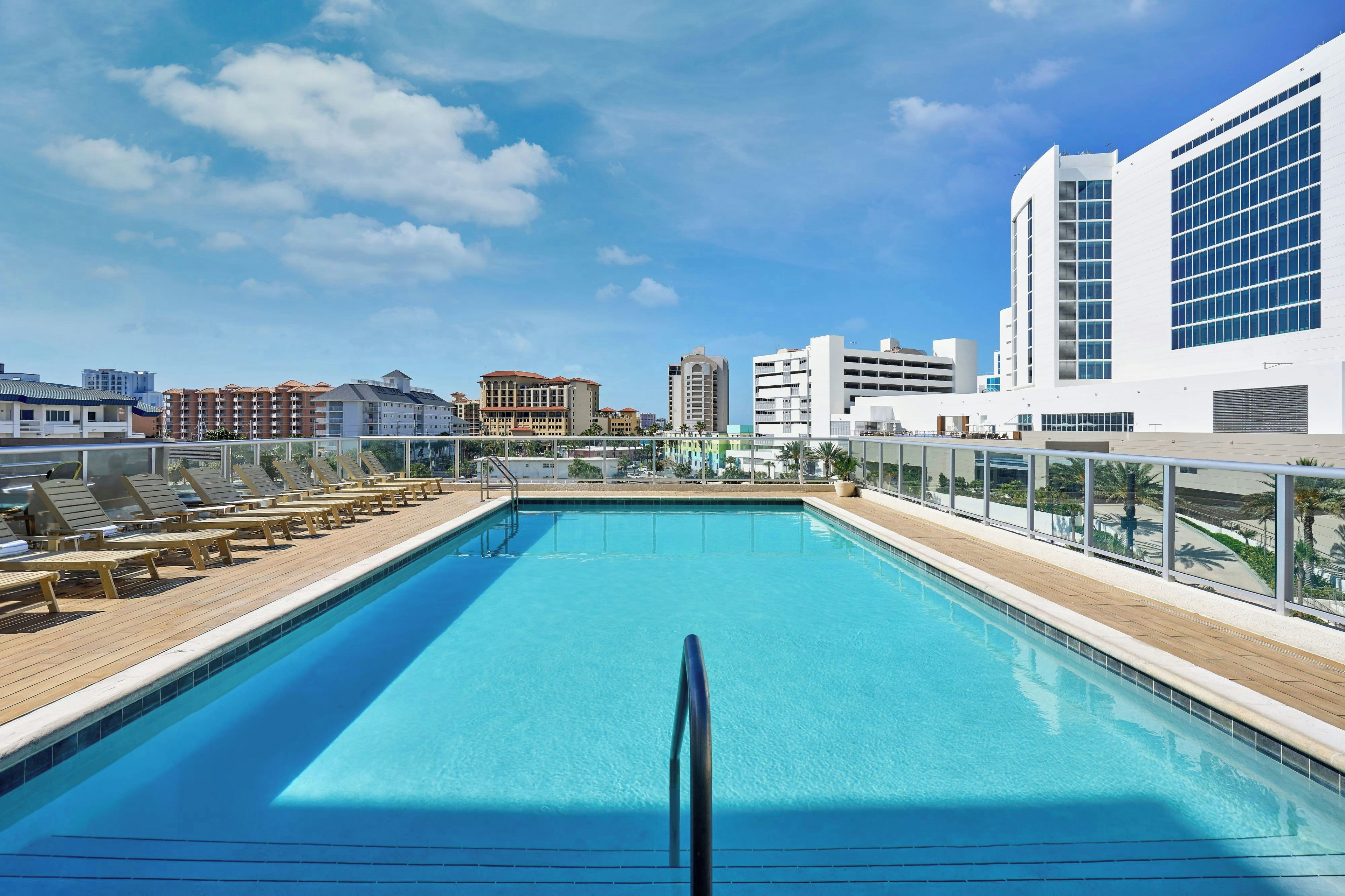 Une piscine sur le toit offrant une vue dégagée sur les gratte-ciel de la ville, entourée de chaises longues et de bâtiments modernes.