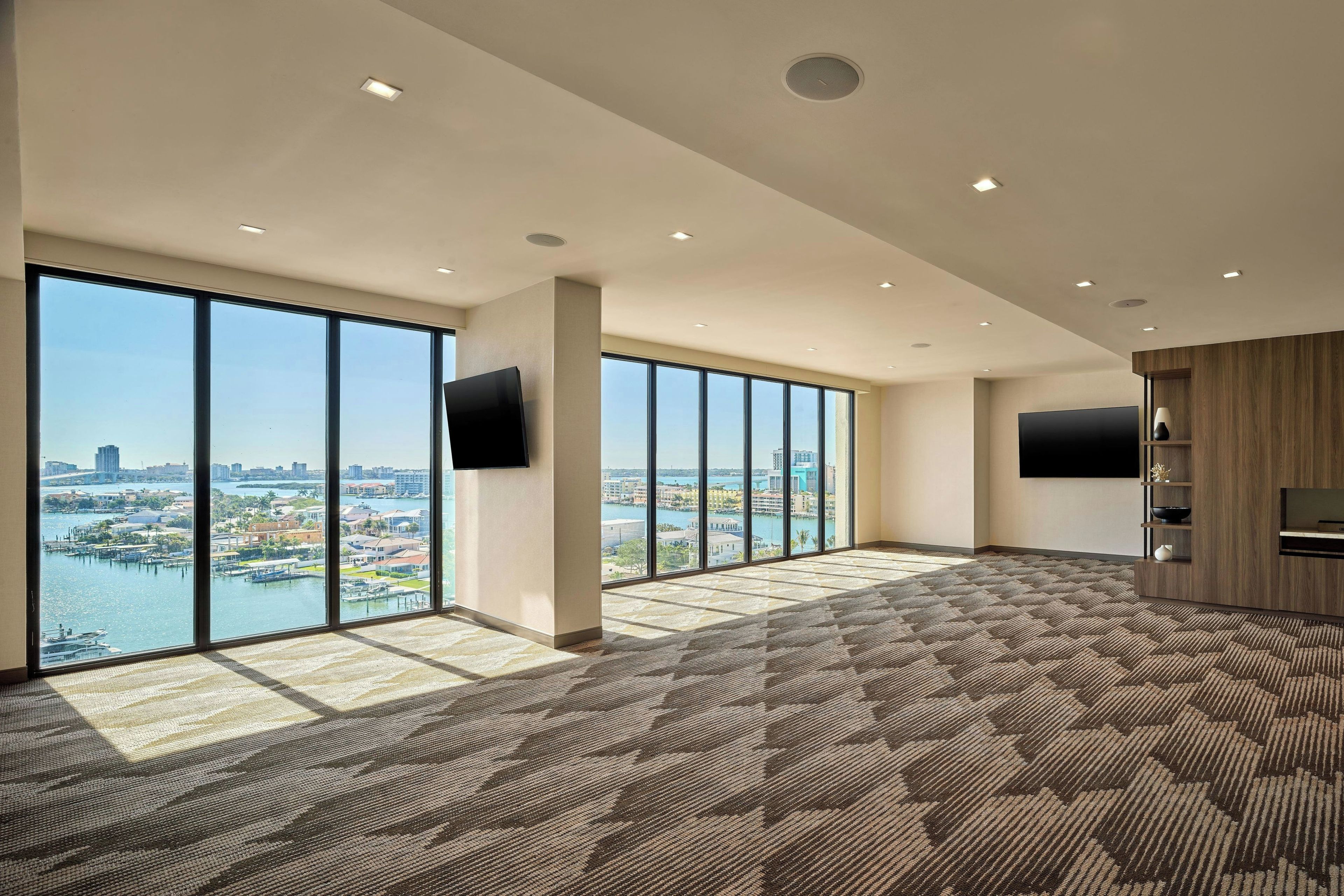 A spacious room with large windows, a flat-screen TV, and a patterned carpet.