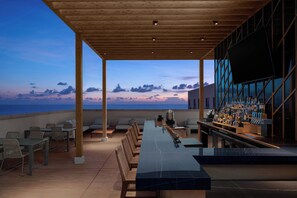 Un bar situé sur le toit, avec une longue table et des chaises, offrant une vue panoramique sur l’océan.