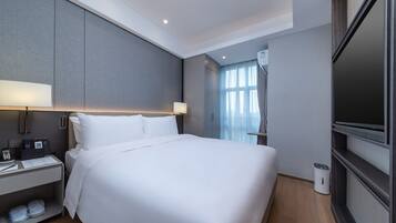 A modern hotel room with a large bed, bedside tables, a TV, and a window with curtains.