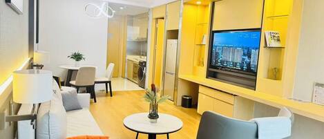 A modern living room with a sofa, chairs, a dining table, a TV, and a kitchen area.