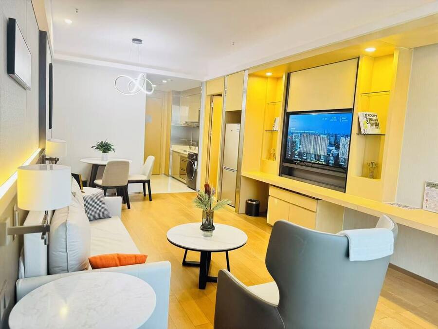A modern living room with a sofa, chairs, a dining table, a TV, and a kitchen area.