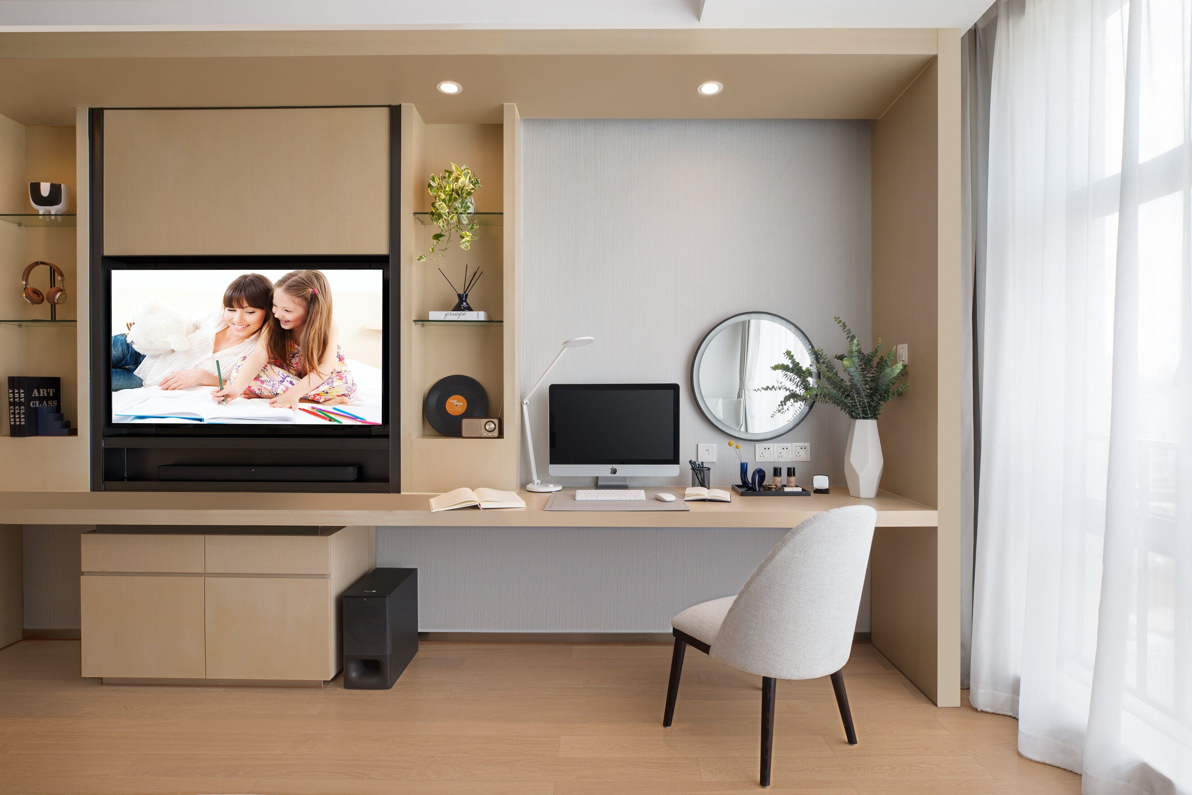 A modern home office with a TV, computer, and desk lamp.