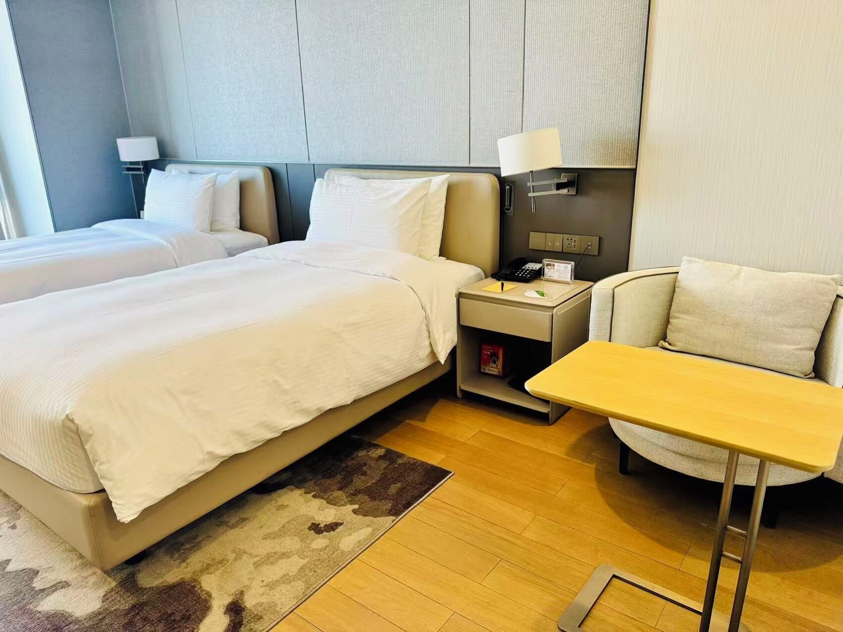 Habitación de hotel con dos camas, un escritorio, una silla, una mesita de noche con lámpara y un teléfono en la pared.