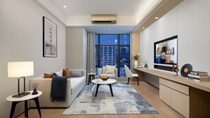 Una sala de estar moderna con un sofá, una mesa de centro y un televisor. Se ve un gran ventanal con vista a la ciudad.